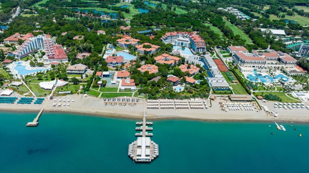 Aerial view of the beachfront resort with multiple buildings, pools, private pier and surrounding greenery.