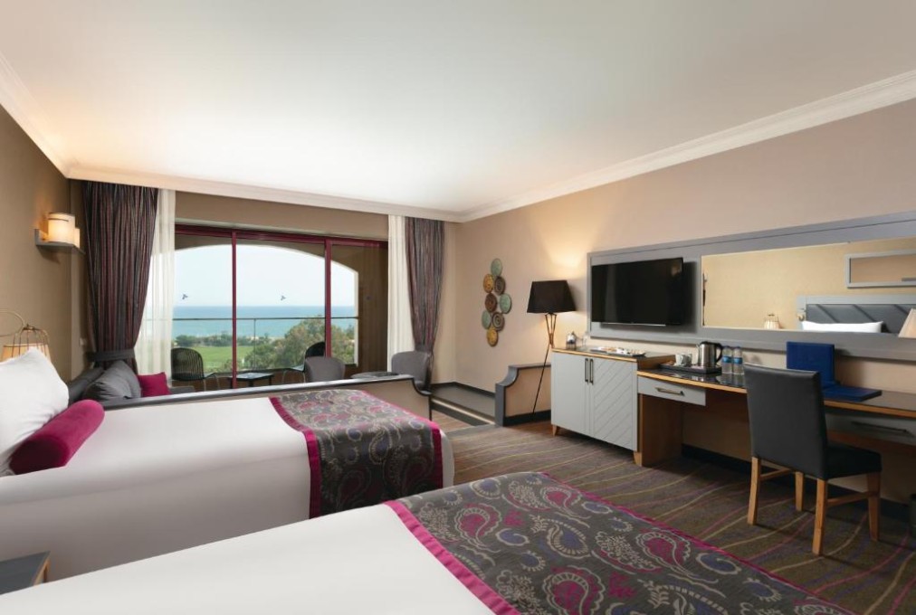 Twin guest room with desk and balcony view toward the sea.