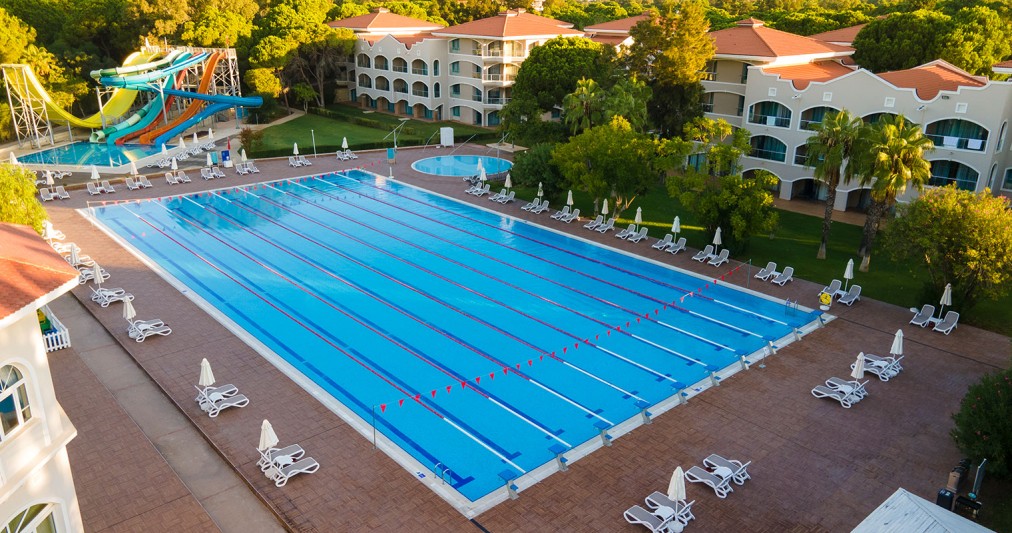 Large outdoor training pool with lap lanes, sun loungers and colorful water slides nearby.