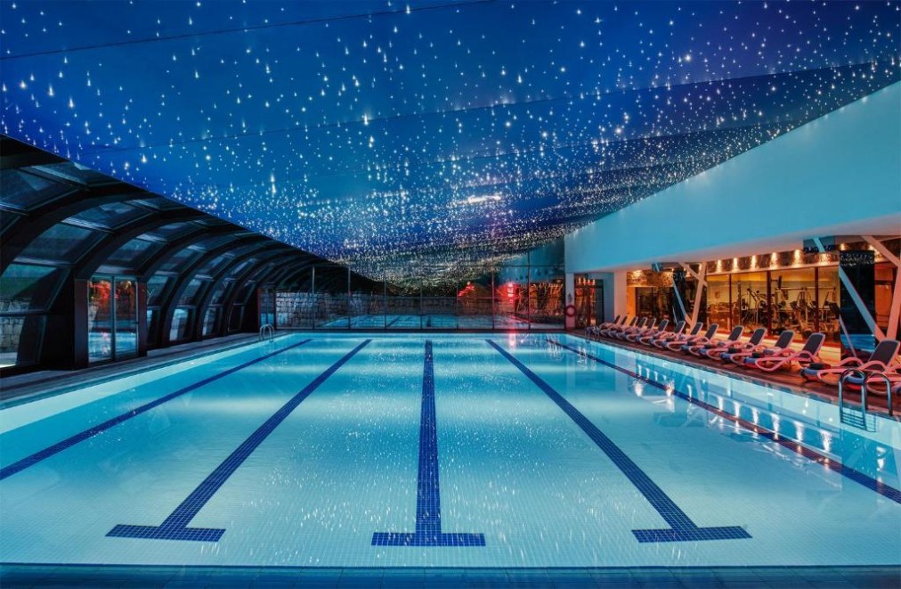 Indoor lap pool with marked swim lanes, lounge chairs and a ceiling filled with star-like lights.