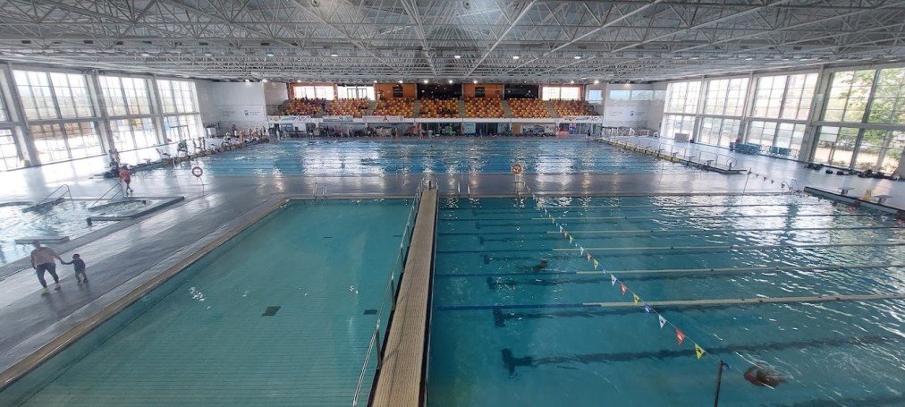 Wide view of an indoor pool complex with lap lanes, a second pool, and a few swimmers.