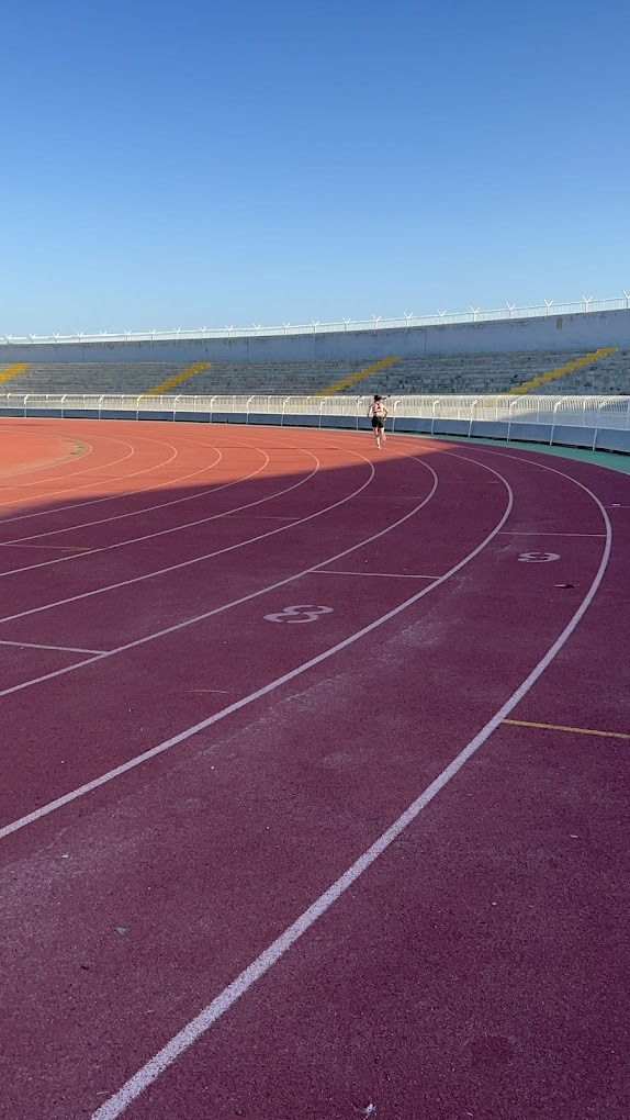 Curved athletics lanes with a person running and empty stadium seating in the background.