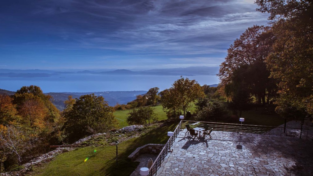 Stone terrace with outdoor seating and panoramic lake and mountain views.
