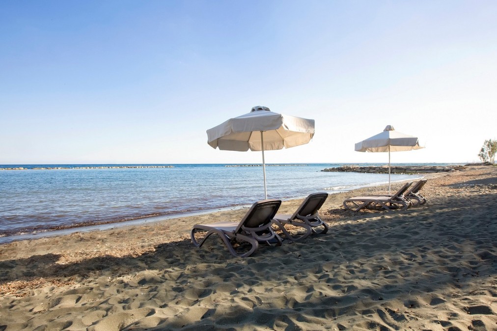 Sandy beach with sun loungers and white umbrellas near calm seaside water
