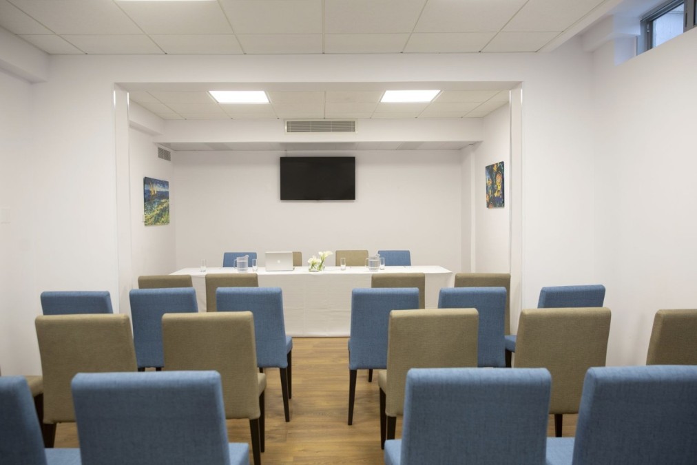 Small conference room with rows of chairs facing table and wall-mounted screen