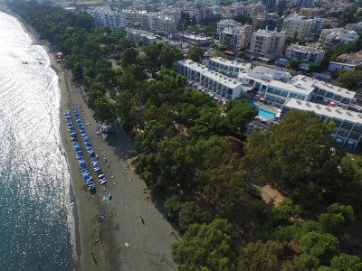 Aerial view of beachfront hotel complex with rows of blue umbrellas and lush trees along the coast