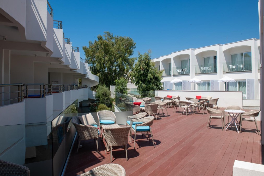 Outdoor hotel terrace with wicker chairs and tables surrounded by white modern buildings