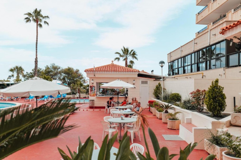 Poolside terrace with bar counter, outdoor tables, umbrellas and seated guests.