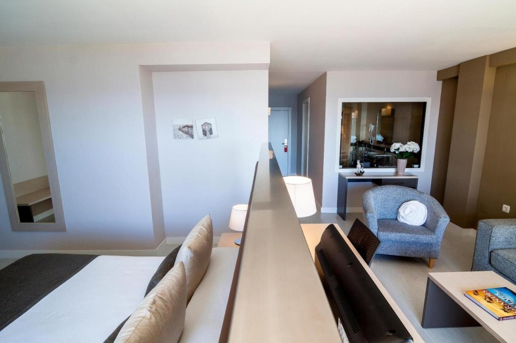 Open-plan room with bed area, lounge chair and interior window to the bathroom.