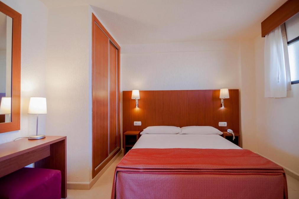 Compact double room with wardrobe, desk and bedside lighting.