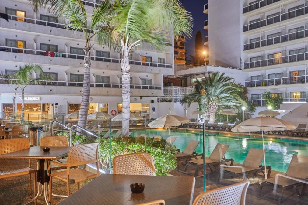 Outdoor pool area at night with loungers, umbrellas, and palm trees.