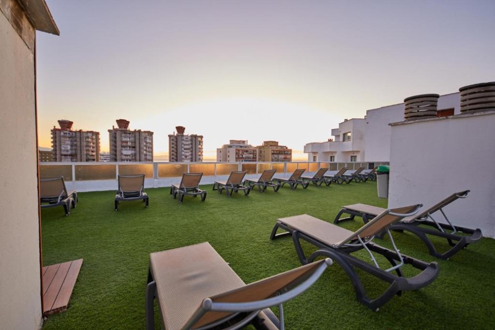 Rooftop sun terrace with loungers on artificial turf and city skyline view at sunset.
