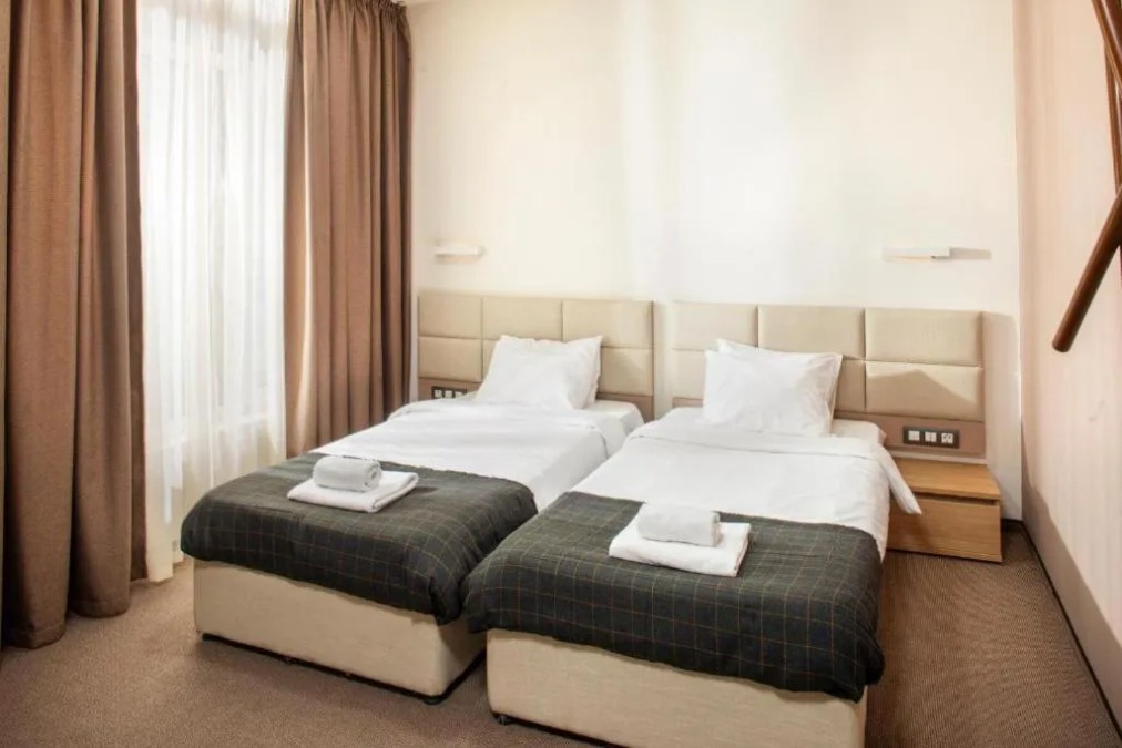 Twin-bed hotel room with bedside tables and towels, team accommodation during sports training camp