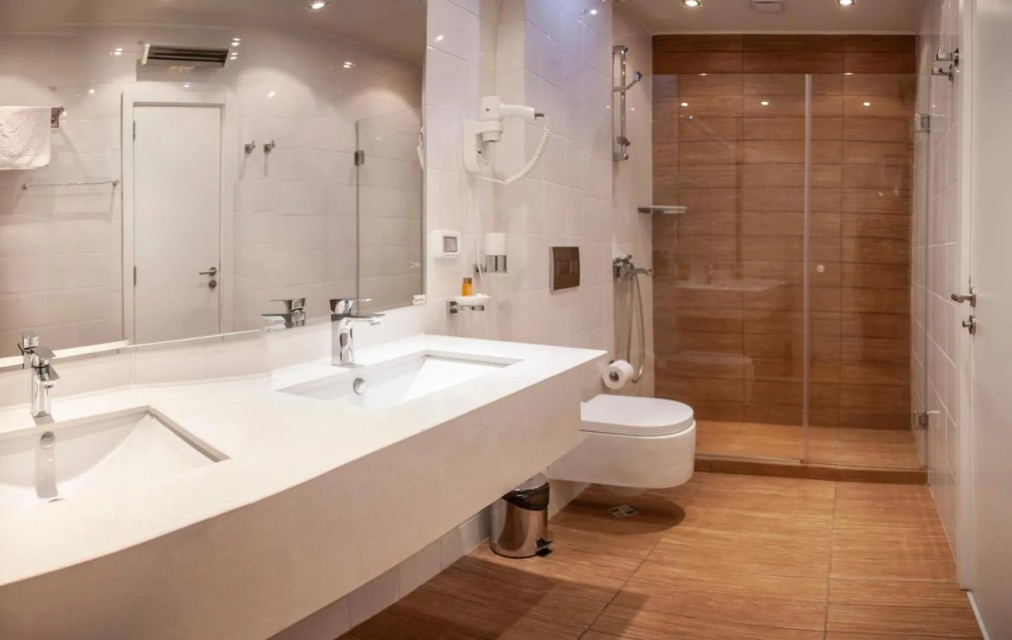 Modern hotel bathroom with double sink, toilet, and walk-in shower, athlete accommodation facilities