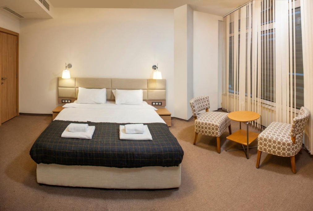 Modern hotel room with double bed, armchairs, and table, athlete lodging during training camp
