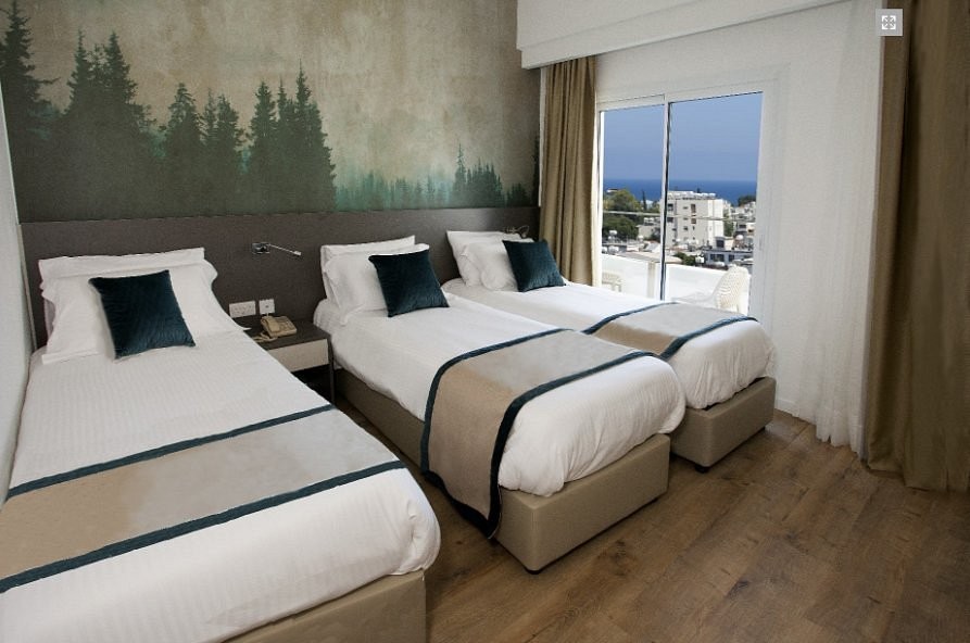 Triple room with three single beds, a forest mural wall and balcony doors with city and sea view.