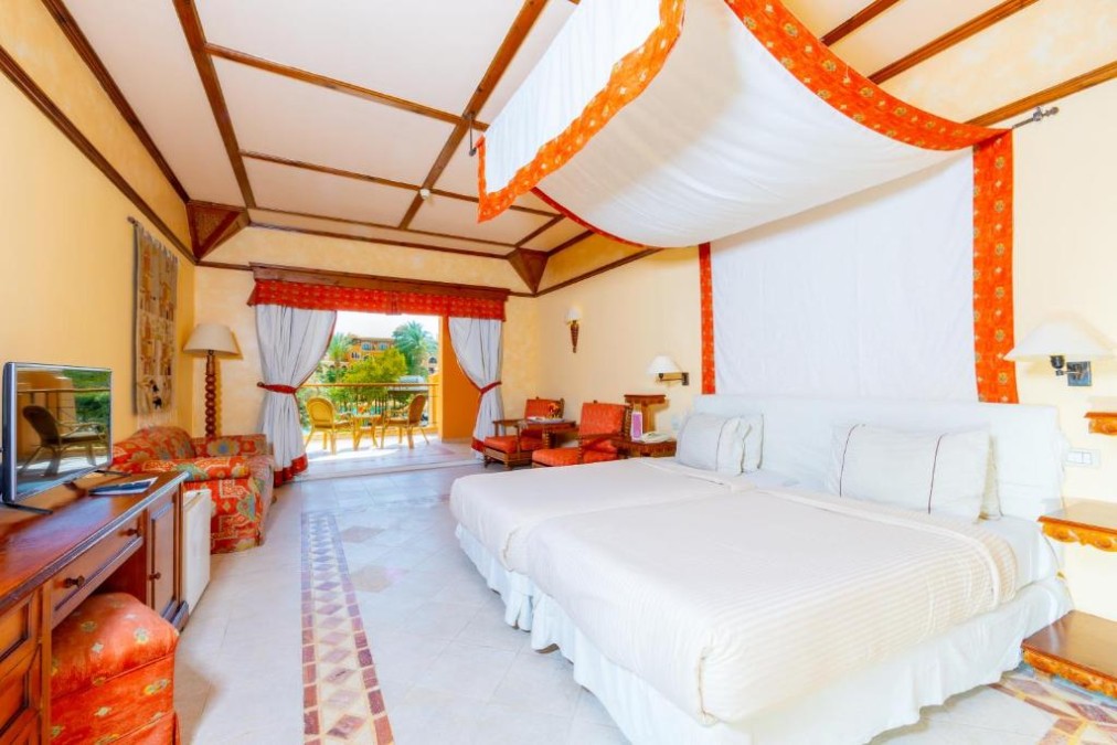 Spacious hotel room with canopy bed, red accents, and balcony access