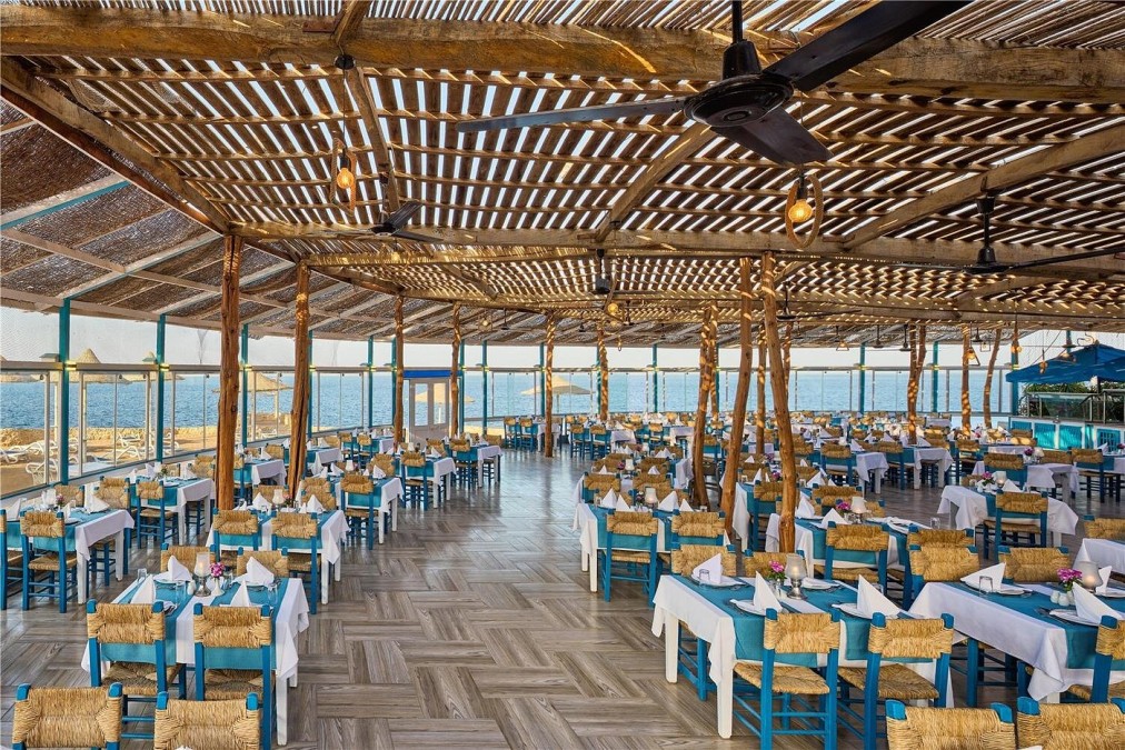 Open-air seaside restaurant with wooden roof, blue chairs, and tables set for dining overlooking the Red Sea