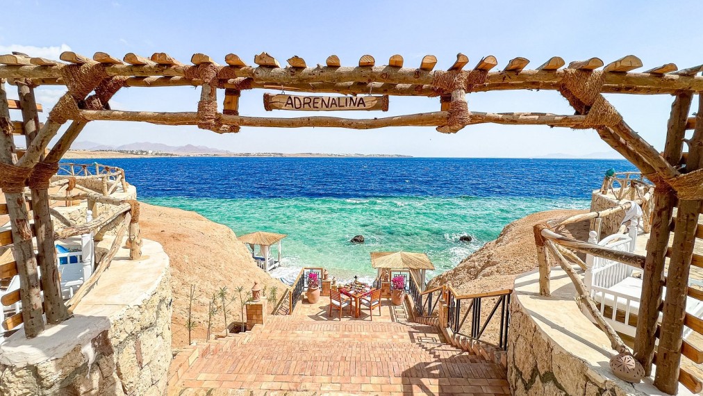 Wooden staircase leading to beach cabanas and turquoise sea under a sign reading “Adrenalina