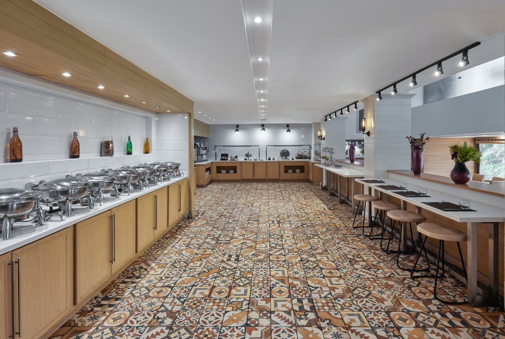 Buffet dining room with chafing dishes, patterned tile floor, and bar seating for training camp meals