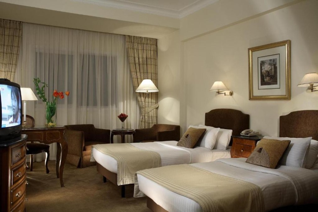 Classic twin room with two beds, TV cabinet, desk, and seating area by the window.