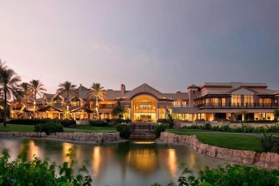 Resort exterior at dusk with illuminated buildings and palm trees reflected in a lagoon.
