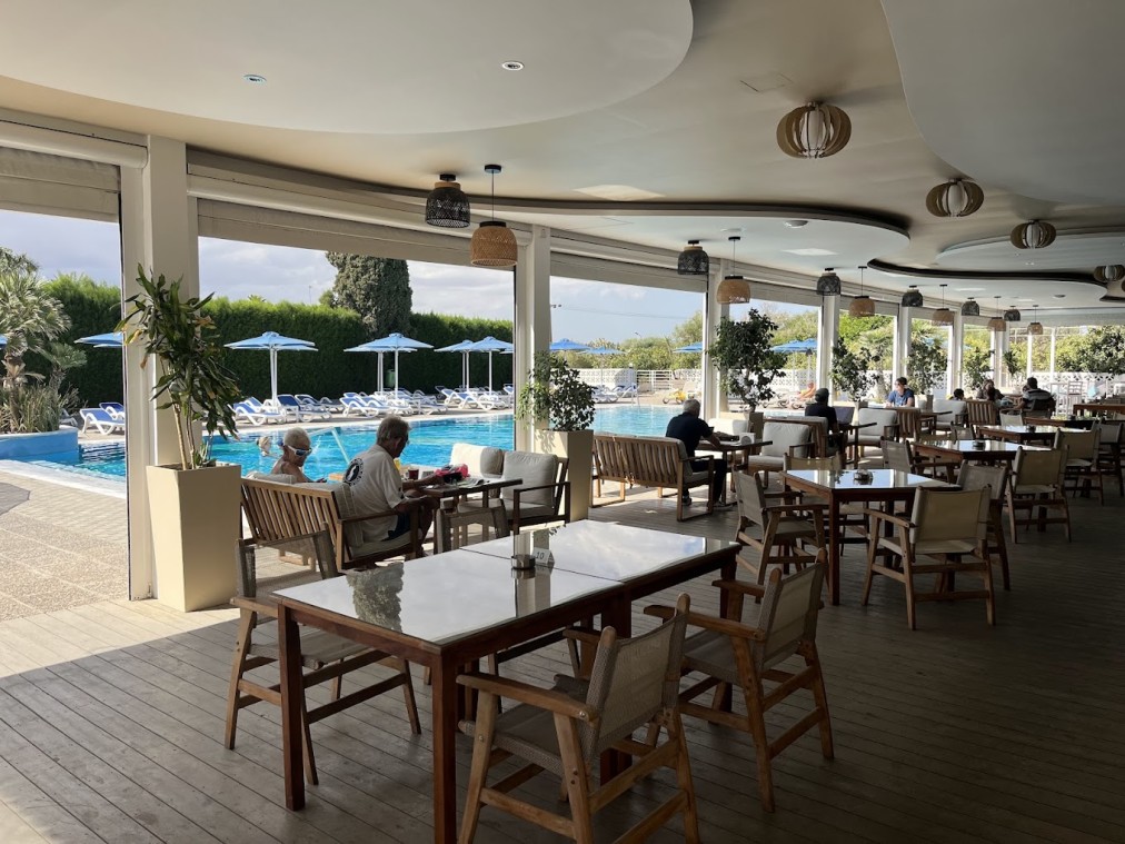 Covered restaurant terrace beside the outdoor pool with tables and seated guests.