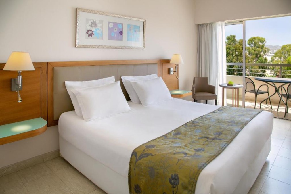 Guest room with double bed, balcony seating and tree view.