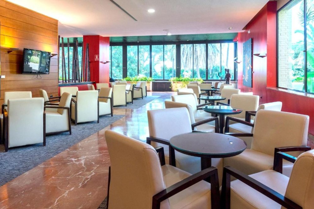 Indoor lounge with armchairs, small tables and large garden-facing windows.