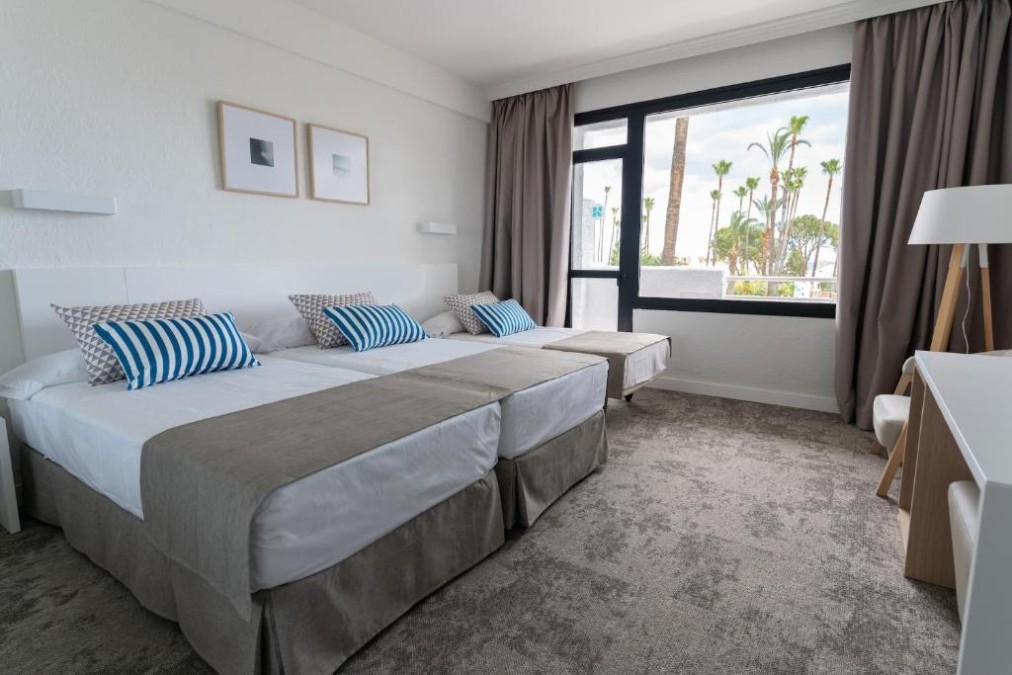 Guest room with three single beds, desk and large window.