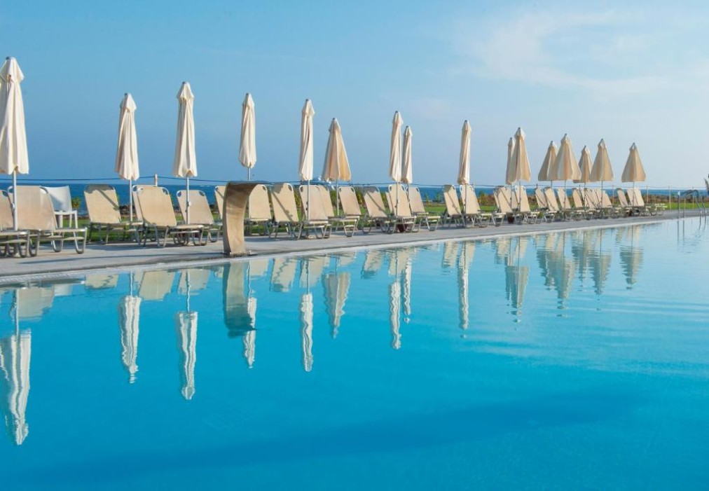 Sun loungers and parasols lined beside a large seafront outdoor pool.