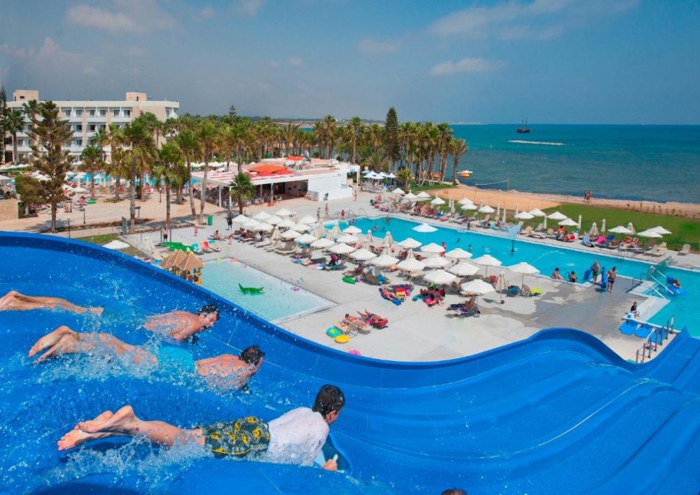 Wide view of waterslides, outdoor pools and seafront hotel grounds.