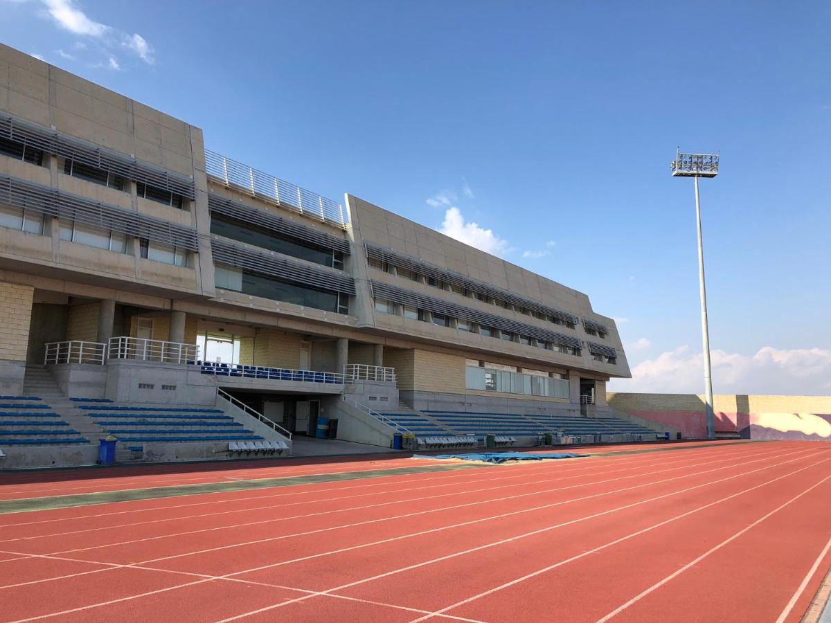 Athletics training facility with red track lanes and seating stands on a sunny day