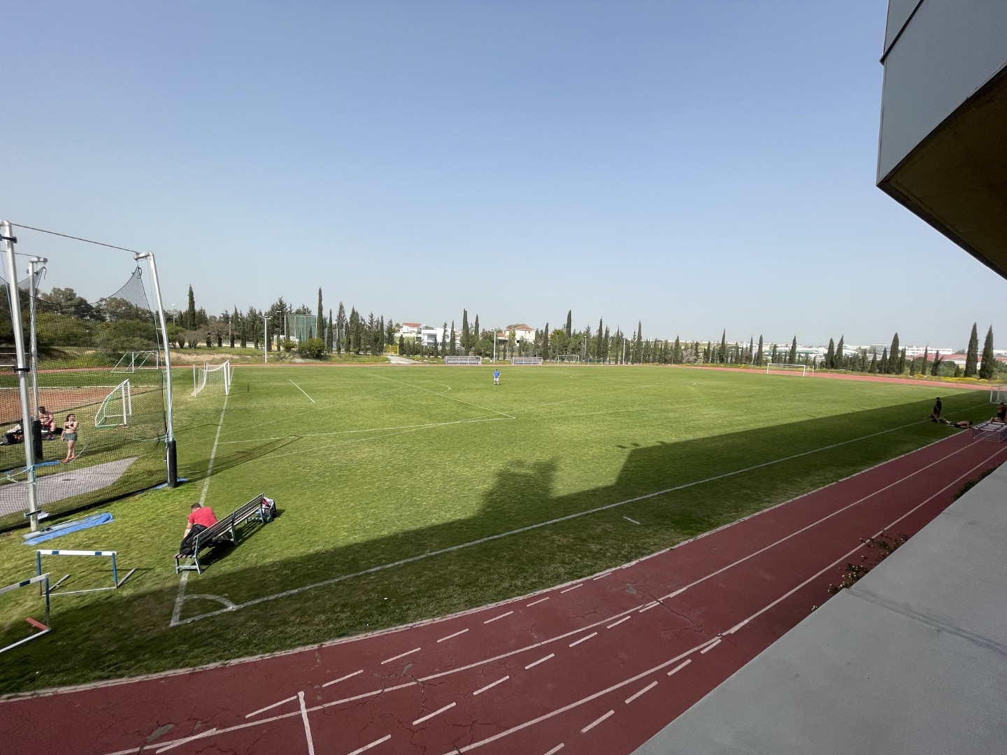 Wide view of grass football field with surrounding red running track and scattered athletes training