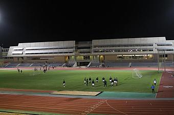 Nachttraining auf einem beleuchteten Leichtathletikfeld mit Spielern, die in der Nähe der Laufbahn trainieren