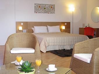 Geräumiges Hotelzimmer mit Doppelbett, Korbstühlen und Couchtisch mit Orangensaft