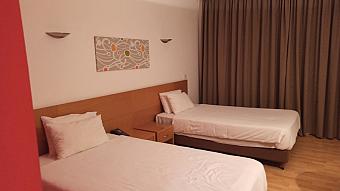 Zweibettzimmer in neutralen Farbtönen mit Holzboden und fensterverdeckendem Vorhang