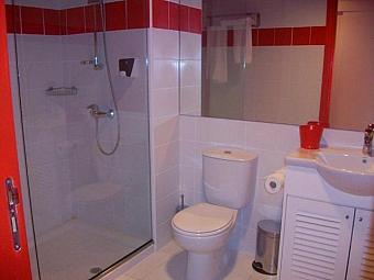 Kompaktes Badezimmer mit begehbarer Dusche, weißen Sanitäreinrichtungen und roten Fliesenakzenten