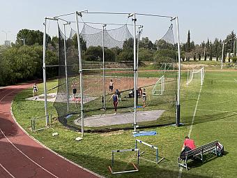 Athleten trainieren Diskus- oder Hammerwurf in einem Netzkäfig auf einem grünen Trainingsfeld