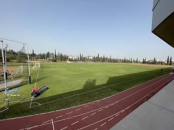 Weitblick auf ein Fußballfeld mit grünem Rasen, umgeben von roter Laufbahn und Athleten, die verstreut trainieren