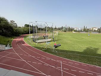 Leichtathletikfeld mit Wurfkäfig, Laufbahnen und grünem Trainingsbereich für Technikübungen in Wurfdisziplinen