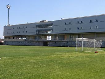 Grünes Fußballtrainingsfeld mit Torpfosten und modernem mehrstöckigem Sportgebäude