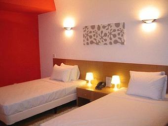 Einfaches Zweibettzimmer mit roter Akzentwand, Nachttischlampen und moderner Einrichtung