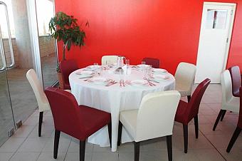 Runder Esstisch mit weißer Tischdecke, roten und weißen Stühlen vor einer hellroten Wand