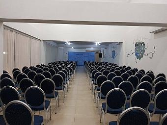 Konferenzraum mit Reihen blauer gepolsterter Stühle, die auf einen Präsentationsbereich ausgerichtet sind
