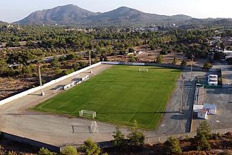Aerial view of green soccer field with goalposts, surrounded by trees and hills, used for training camp practice sessions