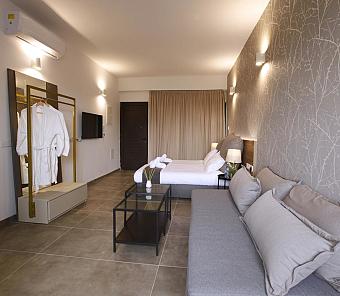 Hotelsuite mit Bett, Sofa und offenem Kleiderschrank in modernem Grau- und Beigeton