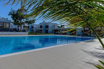 Schwimmbecken mit gefliestem Deck, umgeben von modernen Resortgebäuden und Palmen