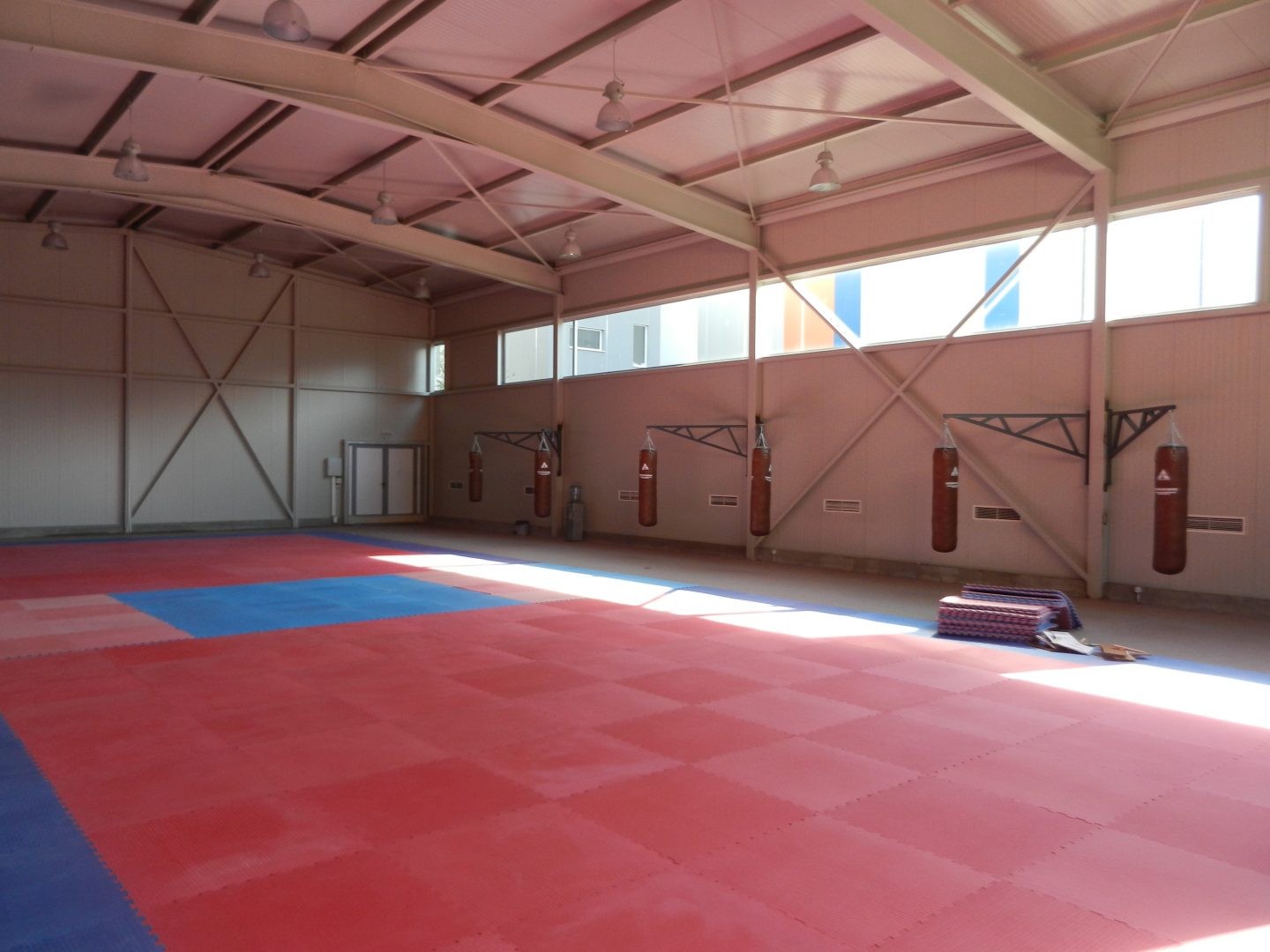 Indoor gym hall with red mat flooring and wall pads, ready for practice sessions