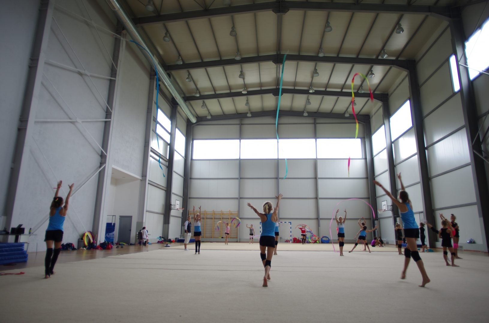 Athletes practicing rhythmic gymnastics with ribbons in a large indoor hall during a training camp session